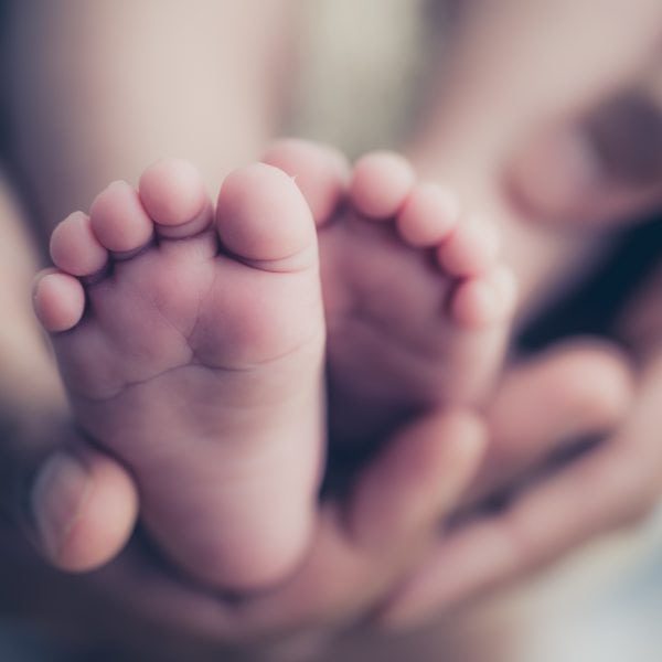 Feet of a newborn baby in the hands of parents. Happy Family oncept. Mum and Dad hug their baby's legs.